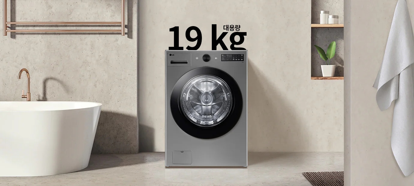 세탁기가 욕실에 놓여 있으며, 세탁기 위에는 19kg 대용량이라는 텍스트가 있습니다. 세탁기 옆에는 욕조와 수건이 걸려 있고, 벽 선반에는 식물과 용기가 놓여 있습니다.