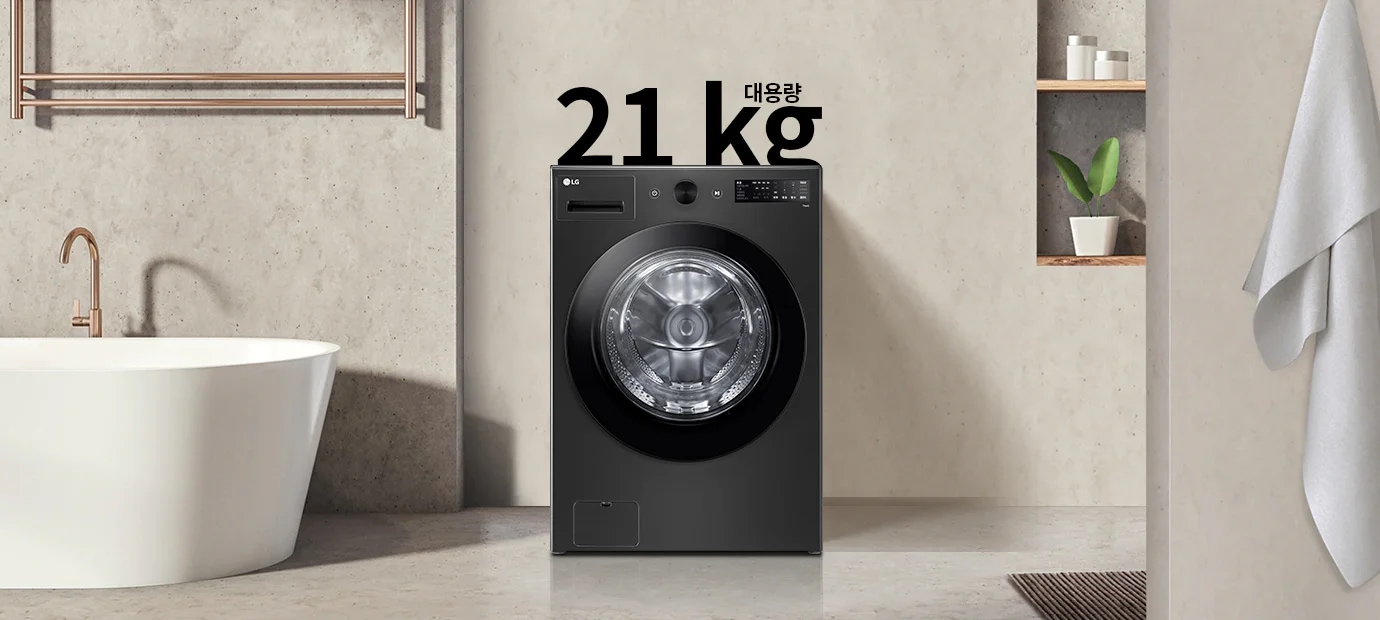 세탁기가 욕실에 놓여 있으며, 세탁기 위에는 21kg 대용량이라는 텍스트가 있습니다. 세탁기 옆에는 욕조와 수건이 걸려 있고, 벽 선반에는 식물과 용기가 놓여 있습니다.