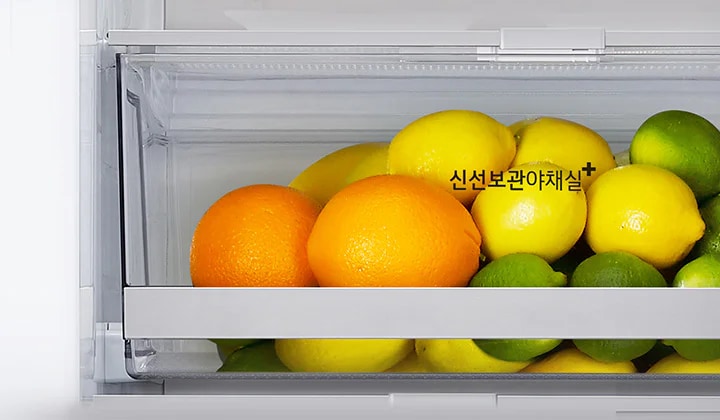 냉장고 내부의 야채 보관실에 오렌지, 레몬, 라임이 담겨 있습니다. 레몬 위에 신선보관야채실이라는 텍스트가 적혀 있습니다.