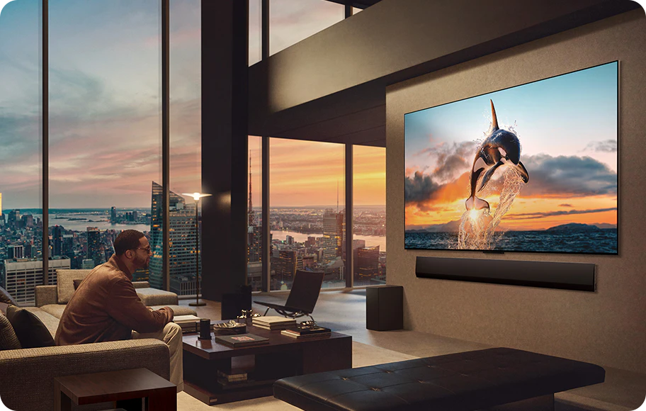도시 풍경을 감상할 수 있는 넓은 거실. LG OLED TV는 LG 사운드바가 있는 벽에 장착되어 있습니다. TV의 원월 디자인으로 벽에 플러시 핏을 맞추고 공간과 잘 어우러집니다. 제로 커넥트 박스는 보이지만 숨겨져 있습니다.