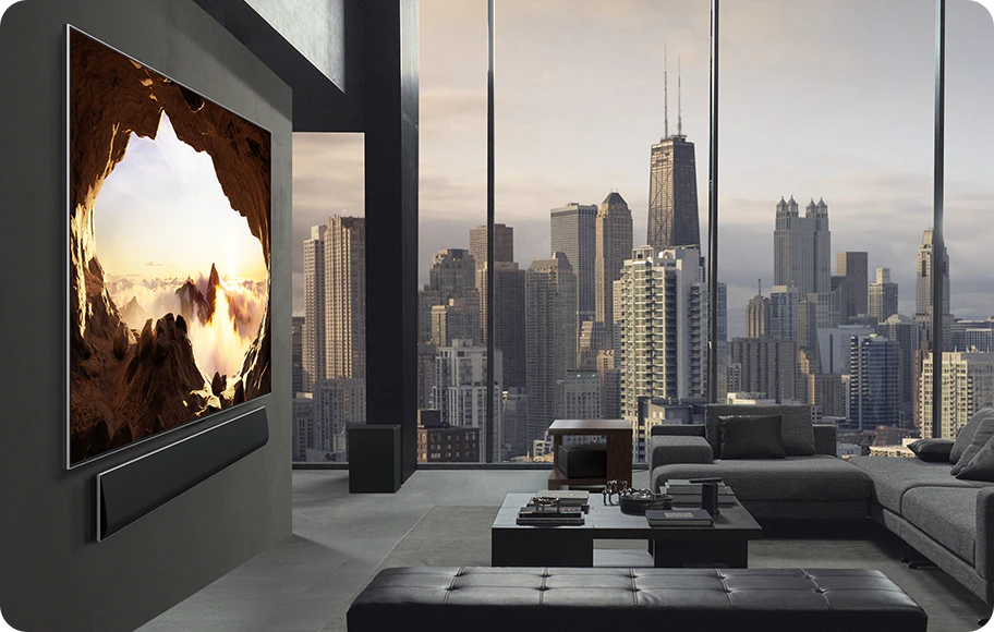 도시 풍경이 보이는 넓은 거실. LG OLED TV는 LG 사운드바가 있는 벽에 장착되어 있습니다. 측면에서 보면 TV의 원월 디자인과 슬림한 베젤이 벽과 공간과 잘 어우러집니다. 제로 커넥트 박스는 보이지만 숨겨져 있습니다.