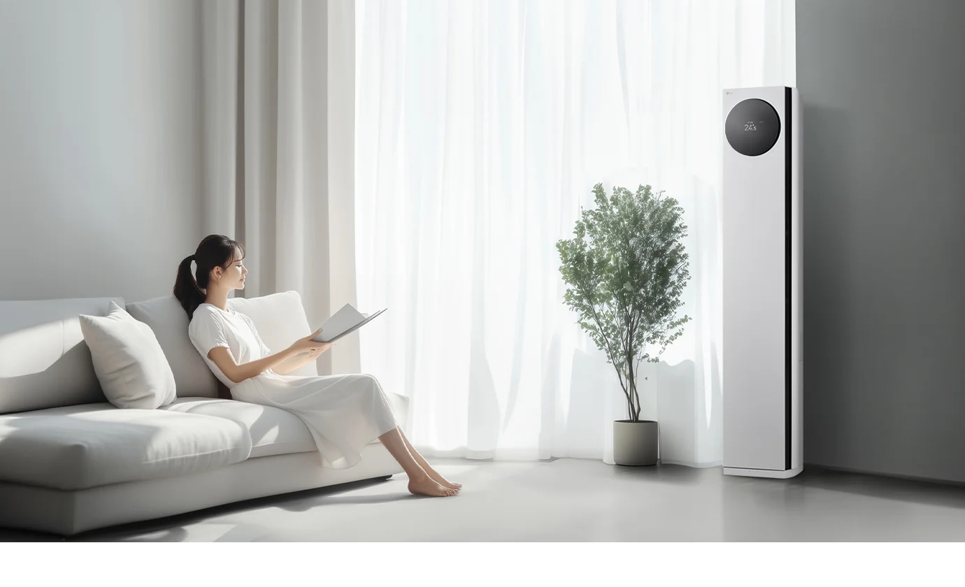 LG 휘센 AI 오브제컬렉션 타워I 에어컨이 오른쪽에 세워져 있으며, 원형 디스플레이에는 24.5°C라는 숫자가 표시되어 있습니다. 에어컨 왼쪽에는 커다란 창문이 있고, 창문을 통해 밝은 자연광이 들어오고 있습니다. 창문 앞에는 화분에 심어진 녹색 식물이 놓여 있습니다. 왼쪽에는 흰색 소파에 앉아 책을 읽고 있는 여성이 보입니다. 그녀는 흰색 원피스를 입고 있으며, 소파에는 흰색 쿠션이 놓여 있습니다.