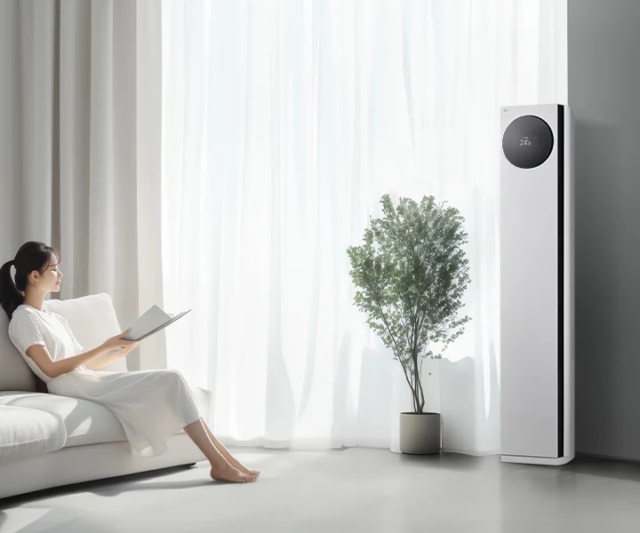 LG 휘센 AI 오브제컬렉션 타워I 에어컨이 오른쪽에 세워져 있으며, 원형 디스플레이에는 24.5°C라는 숫자가 표시되어 있습니다. 에어컨 왼쪽에는 커다란 창문이 있고, 창문을 통해 밝은 자연광이 들어오고 있습니다. 창문 앞에는 화분에 심어진 녹색 식물이 놓여 있습니다. 왼쪽에는 흰색 소파에 앉아 책을 읽고 있는 여성이 보입니다. 그녀는 흰색 원피스를 입고 있으며, 소파에는 흰색 쿠션이 놓여 있습니다.