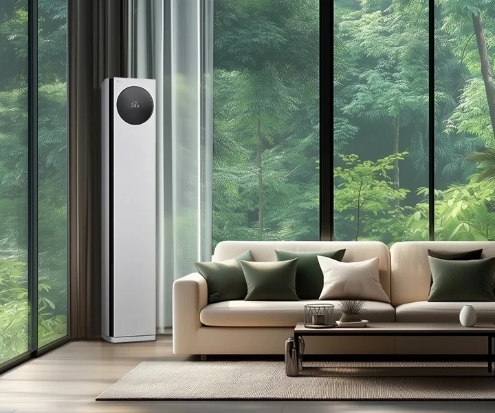 LG 휘센 AI 오브제컬렉션 타워I 에어컨이 거실의 왼쪽 구석에 세워져 있으며, 에어컨의 원형 디스플레이에는 24.5°C라는 숫자가 표시되어 있습니다. 에어컨 옆으로는 큰 창문이 있어 푸른 숲의 풍경이 보이며, 창문 앞에는 베이지색 소파가 놓여 있습니다. 소파 위에는 여러 개의 녹색과 흰색 쿠션이 배열되어 있고, 소파 앞에는 낮은 테이블이 놓여 있습니다. 테이블 위에는 장식품과 책이 놓여 있으며, 오른쪽에는 큰 화분에 심어진 녹색 식물이 배치되어 있습니다.