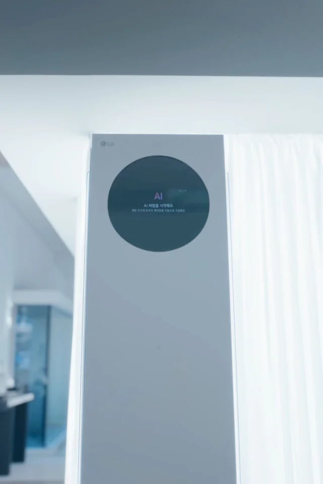 스탠드 에어컨의 상단 전면이 클로즈업되어 보이며, 원형 블랙 디지털 디스플레이 영역 중앙에는 AI 라는 표시가 있고, 그 아래에 AI 바람을 시작해요 라는 문구가 나타나 있습니다. 하단에는 희망 온도에 맞추어 쾌적함을 자동으로 조절해요라는 안내 문구가 작은 글씨로 표시되어 있습니다. 이 이미지는 에어컨의 AI바람 기능이 작동을 시작했음을 사용자에게 알리는 상태 표시 화면을 설명합니다.
