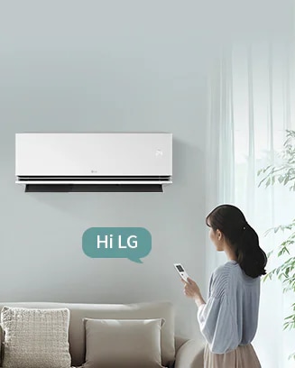 벽에 설치된 LG 휘센 오브제컬렉션 듀얼쿨 벽걸이에어컨이 보입니다. 오른쪽에는 Hi LG라는 말풍선이 있으며, 왼쪽에는 스마트폰을 들고 있는 여성이 서 있습니다. 여성은 창문 쪽을 바라보고 있으며, 창문을 통해 부드러운 자연광이 들어옵니다. 소파는 크림색으로, 여러 개의 쿠션이 놓여 있습니다. 소파 뒤에는 커튼이 드리워져 있고, 왼쪽에는 화분이 놓여 있습니다.