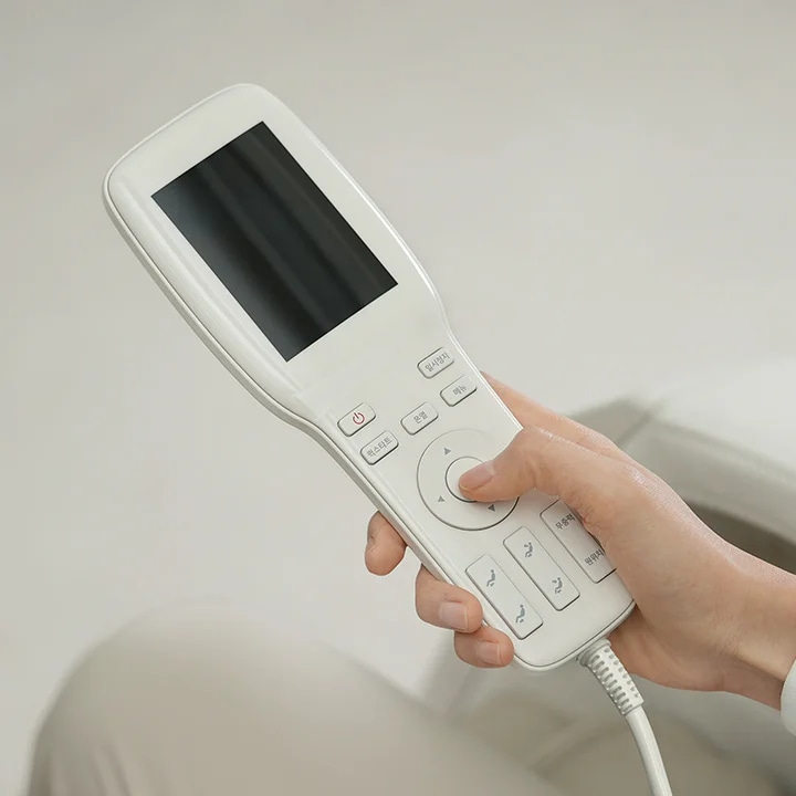 손이 흰색 리모컨을 잡고 있으며, 리모컨에는 작은 화면과 여러 개의 버튼이 있습니다. 버튼에는 전원, 온도, 모니터, 원상복귀, 메뉴, 무중력, 무중력 해제 등의 텍스트가 적혀 있습니다. 배경은 밝은 색상으로 되어 있습니다.