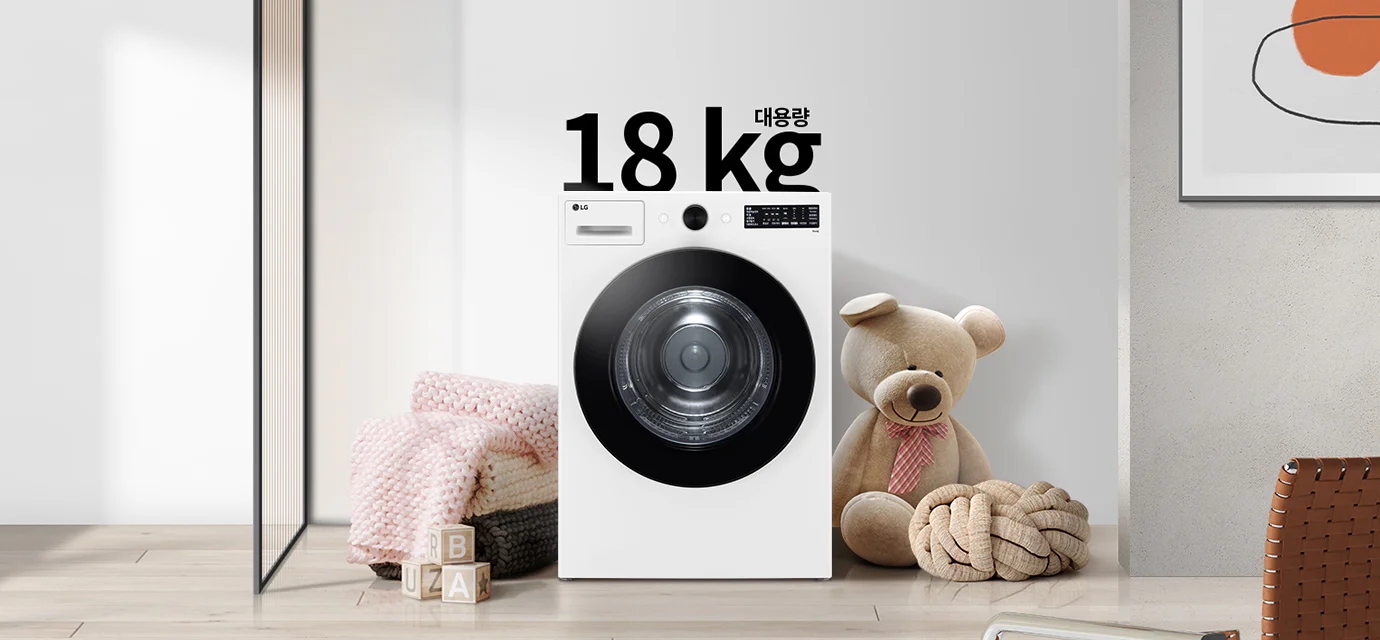 세탁기가 놓여 있으며, 18 kg 대용량이라는 문구가 있습니다. 세탁기 옆에는 곰 인형과 두꺼운 니트 담요가 놓여 있고, 바닥에는 알파벳 블록이 있습니다. 벽에는 추상적인 그림이 걸려 있습니다.